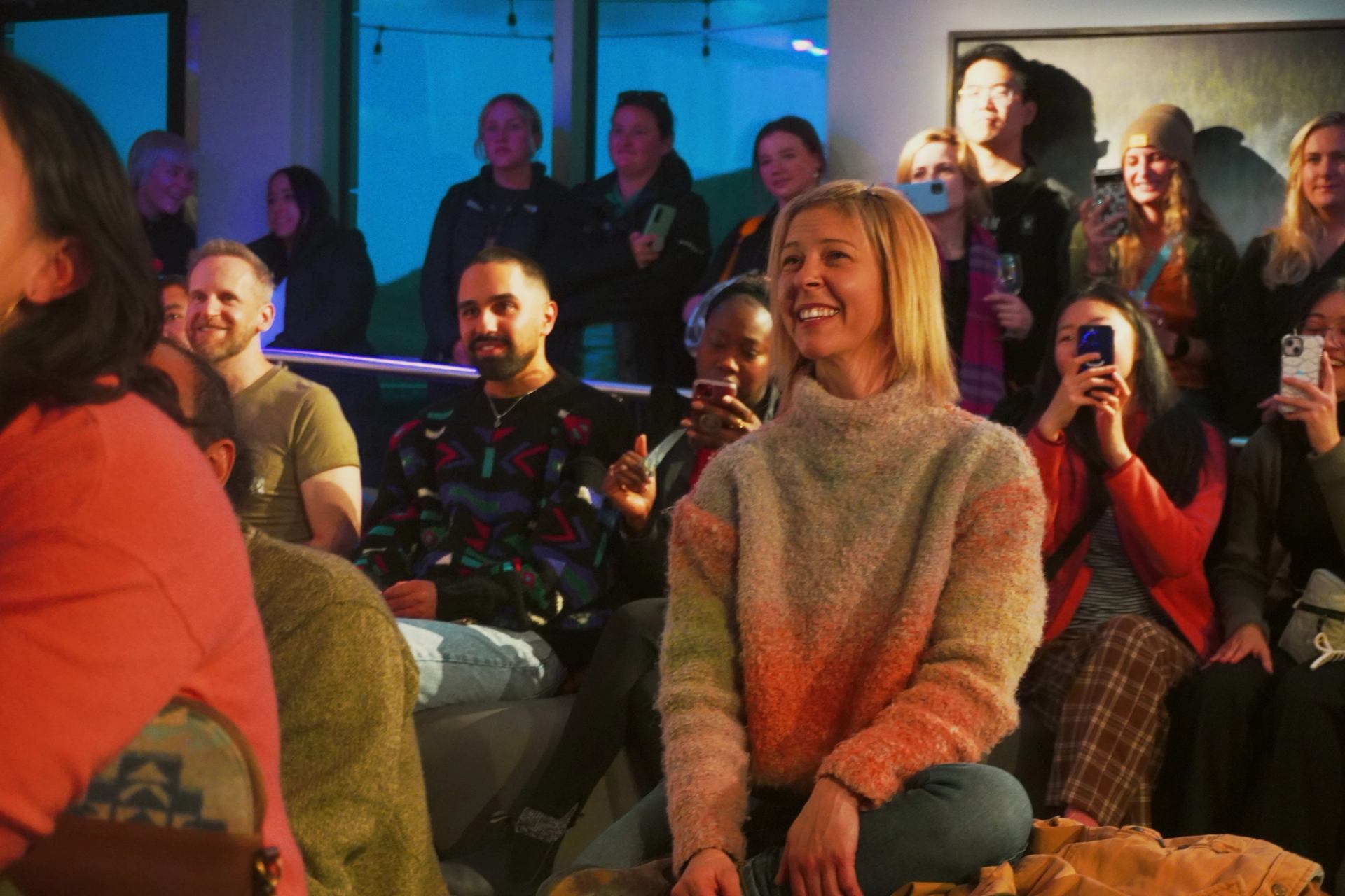 Group of people gathered indoors at an event, with some seated and others standing.