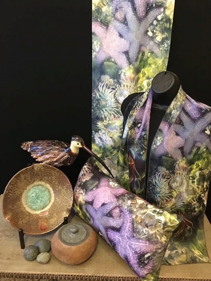 Ceramic bird sculpture, bowls, and glass art on display beside patterned textile background.