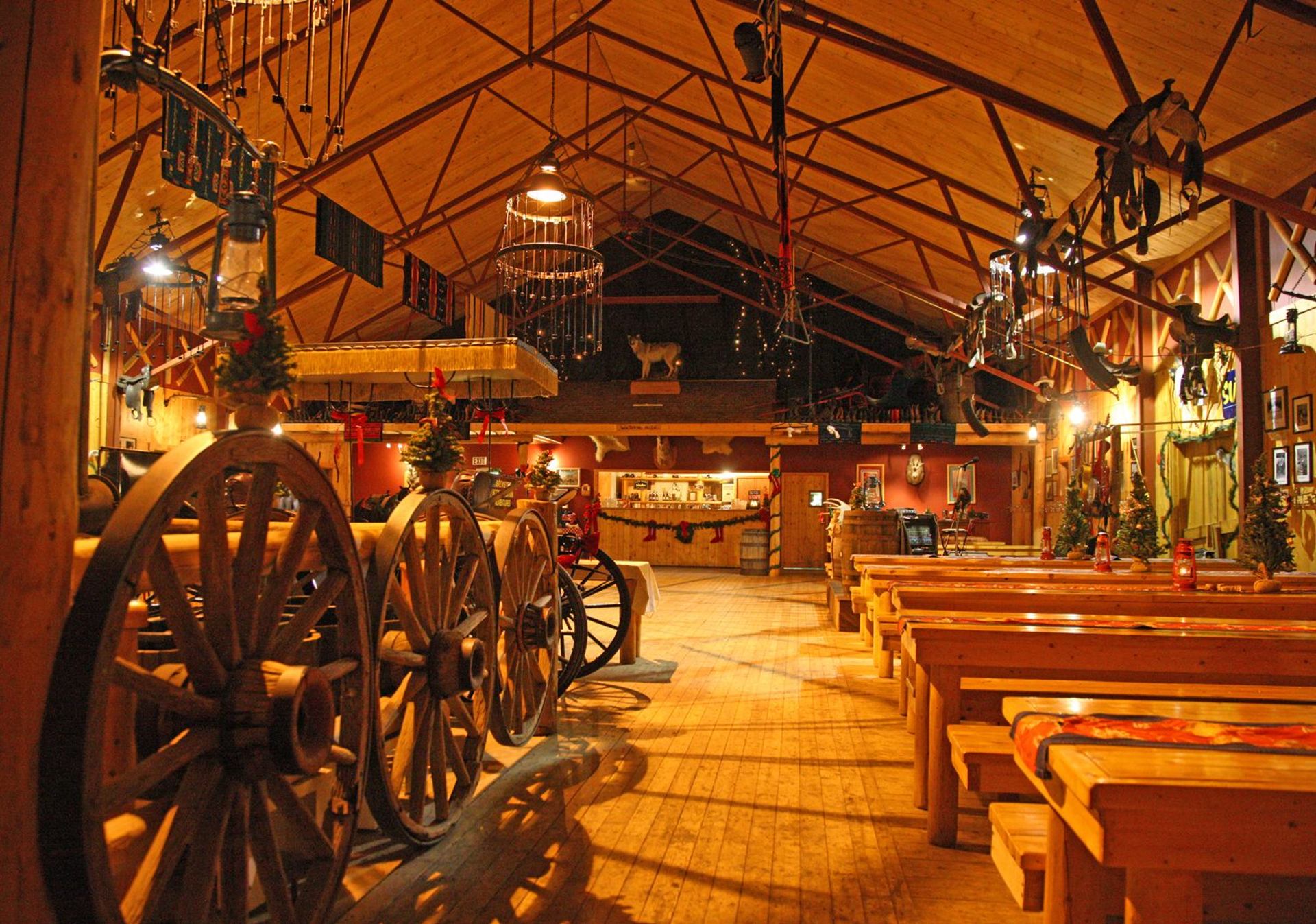 Rustic lodge dining hall with wooden tables, wagon wheel décor, lanterns, and Western-style accents.