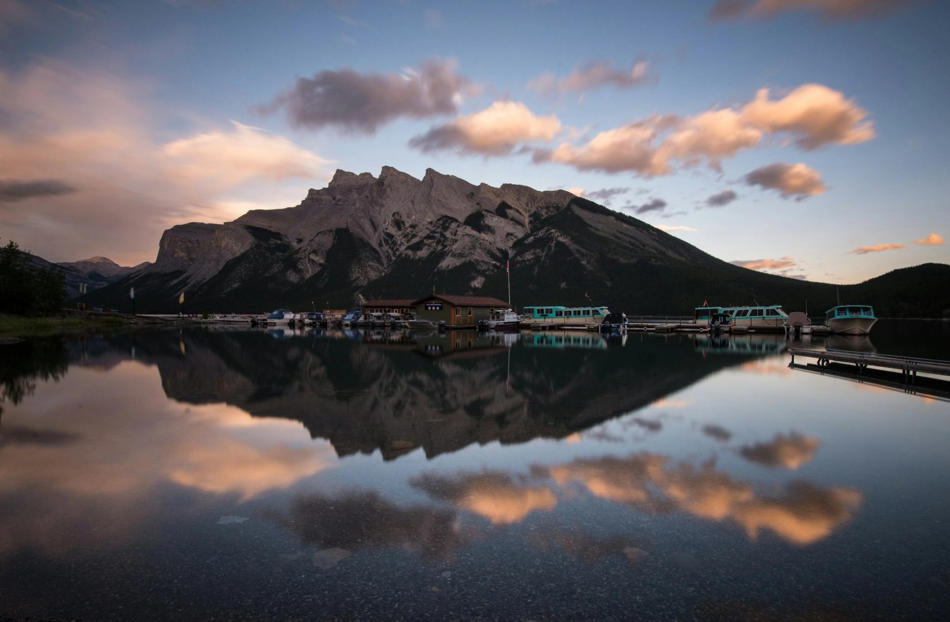 Mountain lake with boats at docks and clouds reflected in calm water.