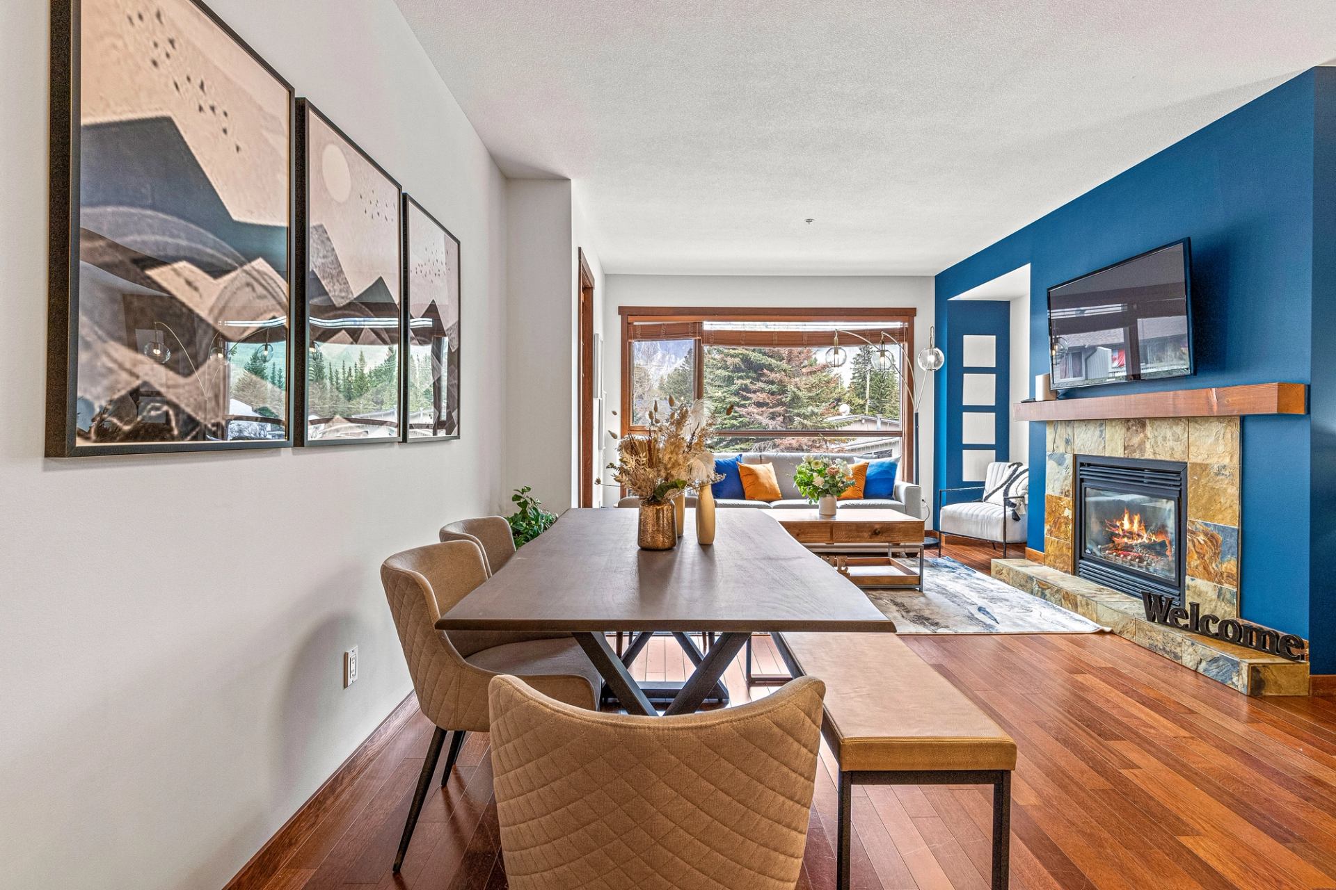 Modern dining and living room with blue accent wall, fireplace, and large windows.