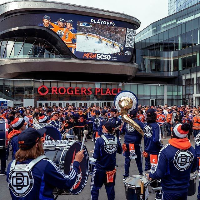 Drumline performs before crowd outside Rogers Place under large hockey playoff screen.
