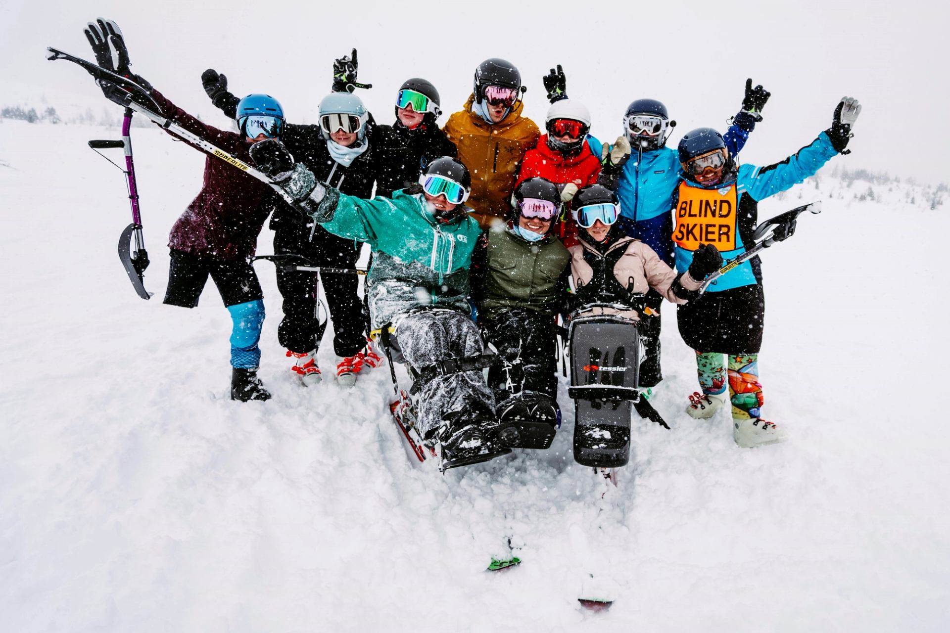 Group in winter gear posing on snow, including a blind skier.