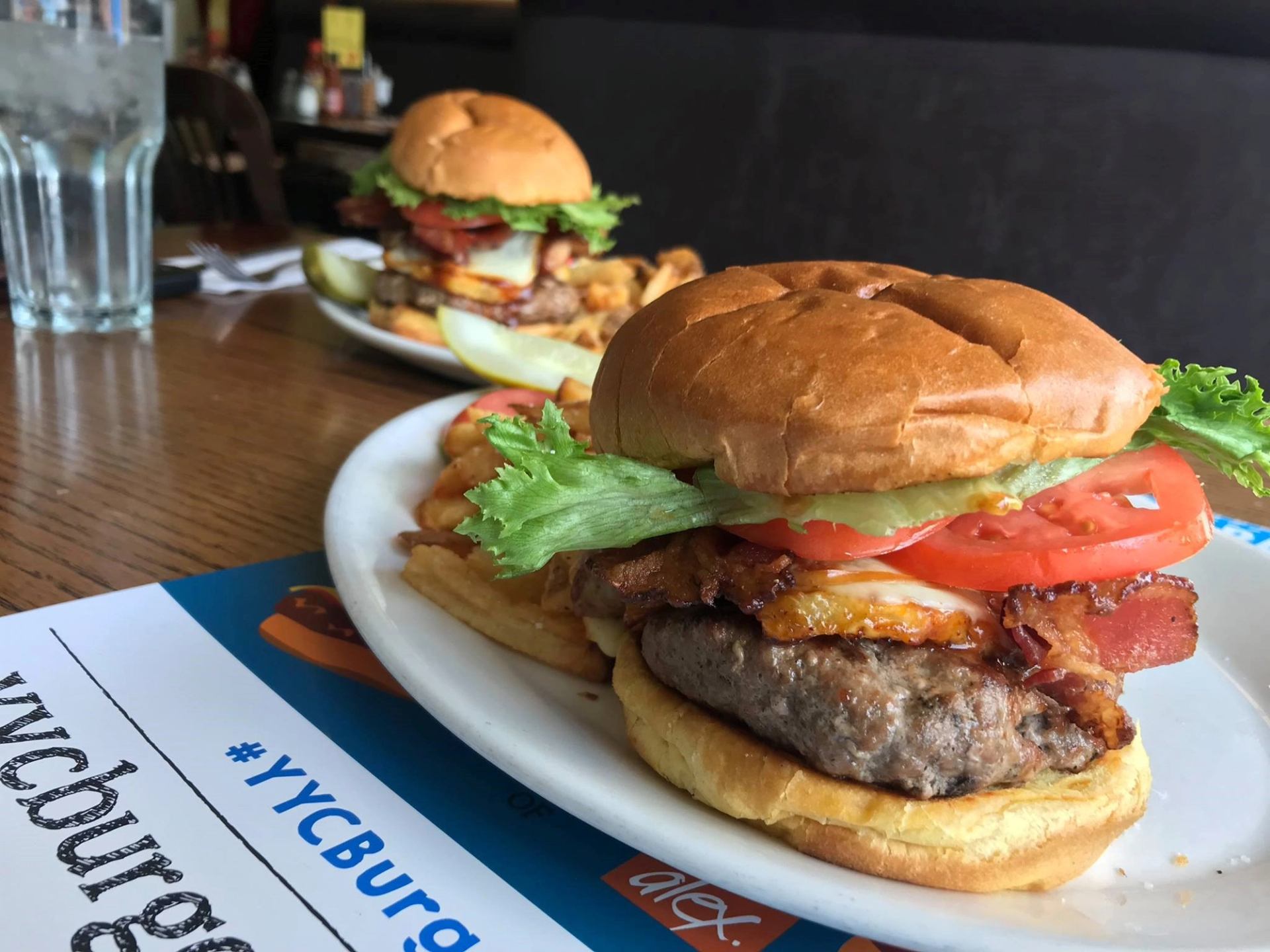 Close-up of a bacon cheeseburger with lettuce and tomato on a white plate.