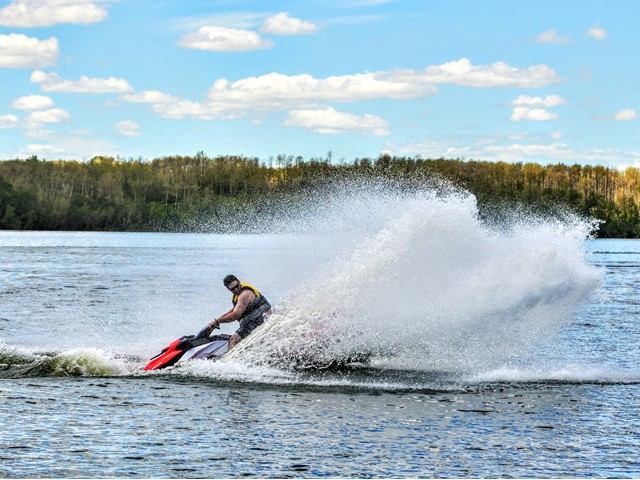 Person riding a jet ski, splashing water on a sunny lake day.