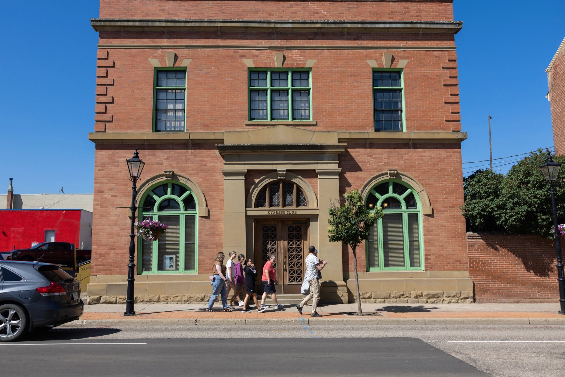 Historic brick Cypress Club building with green-trimmed windows and pedestrians walking past.
