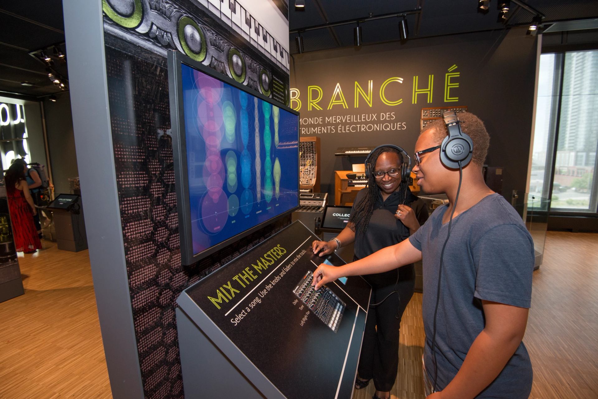 Visitors wearing headphones use interactive music mixing display in electronic instruments exhibit.