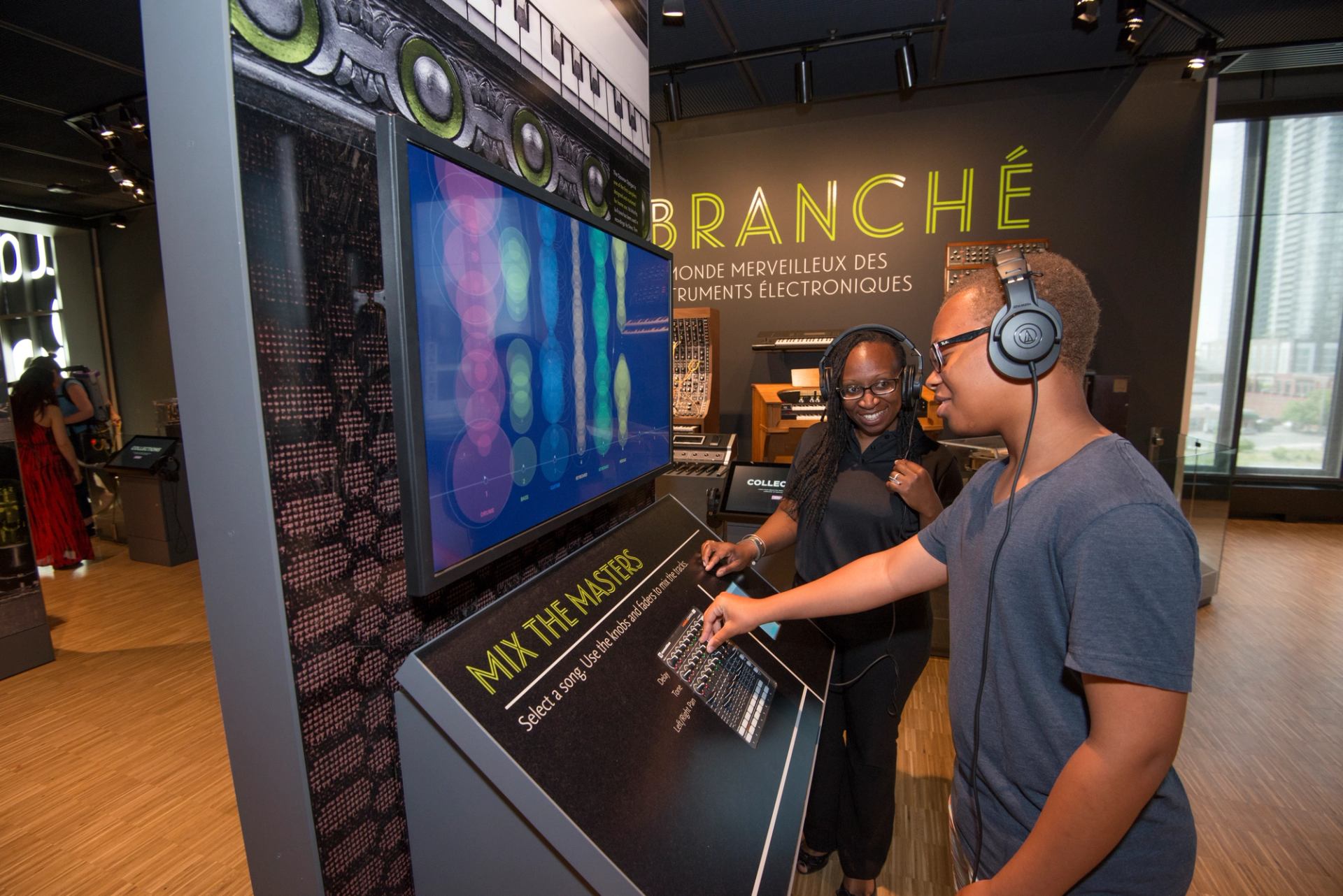 Visitors wearing headphones use interactive music mixing display in electronic instruments exhibit.