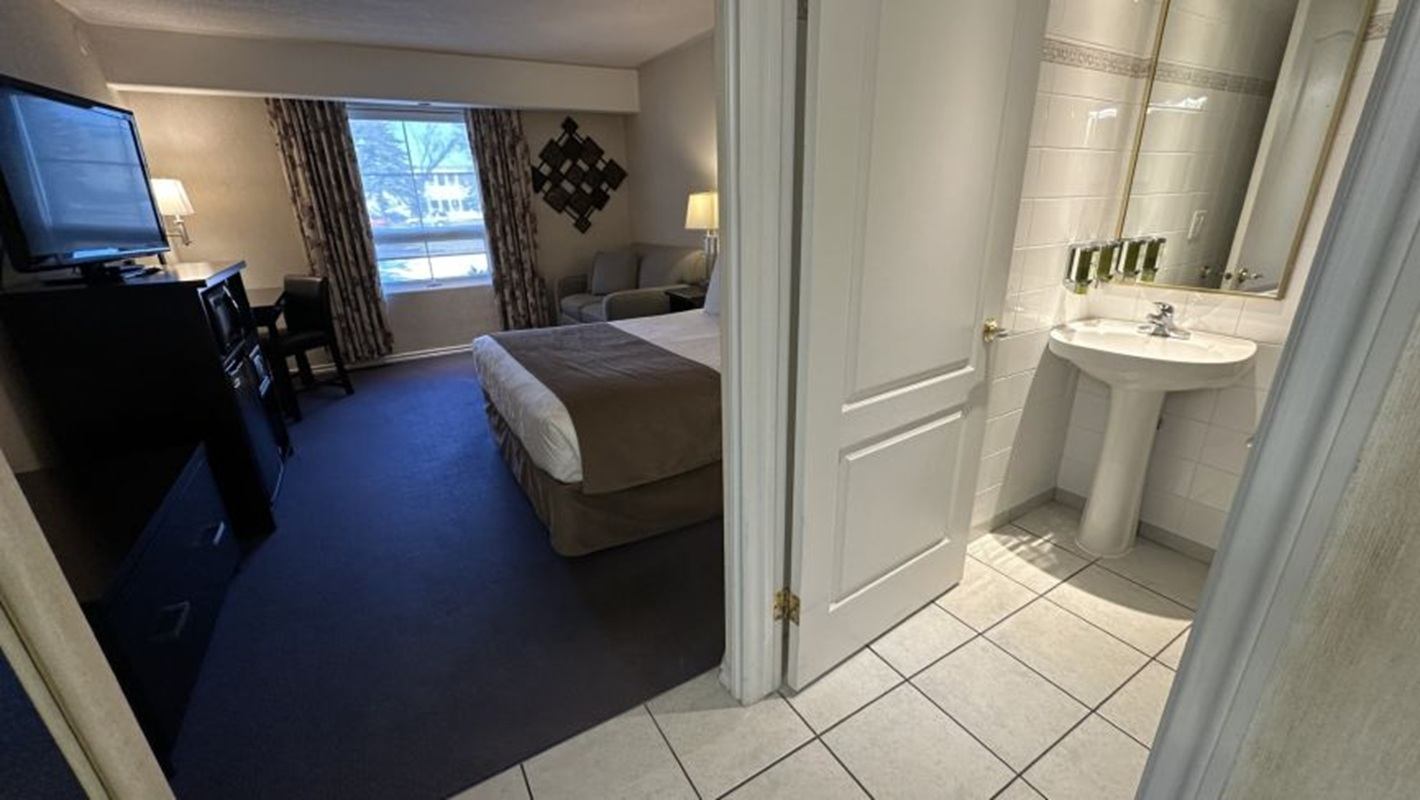 Hotel room with bed, sofa and desk beside open door to tiled bathroom.