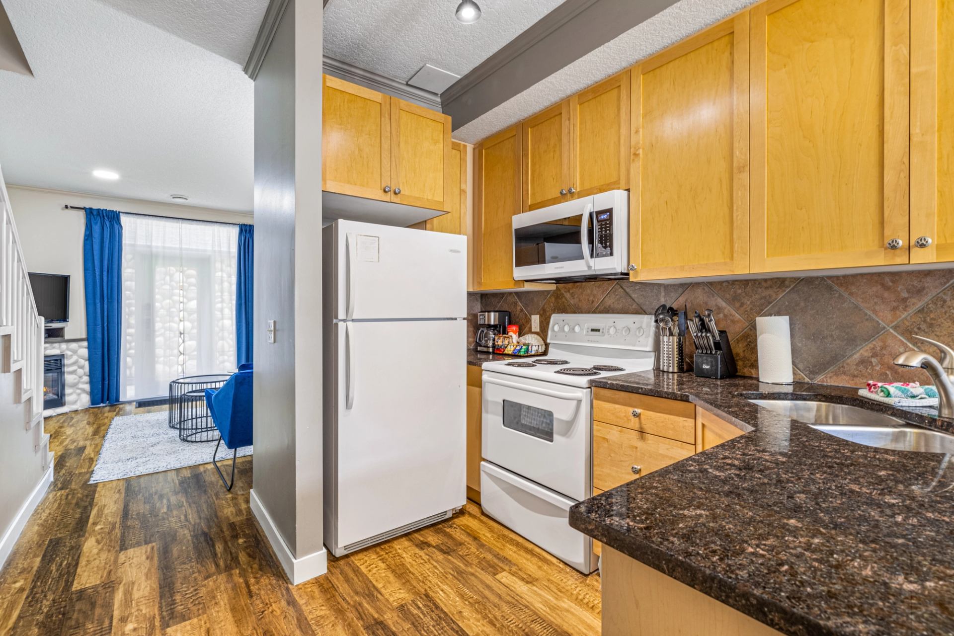 Kitchen with wood cabinets, dark counters, white appliances and adjoining living area.