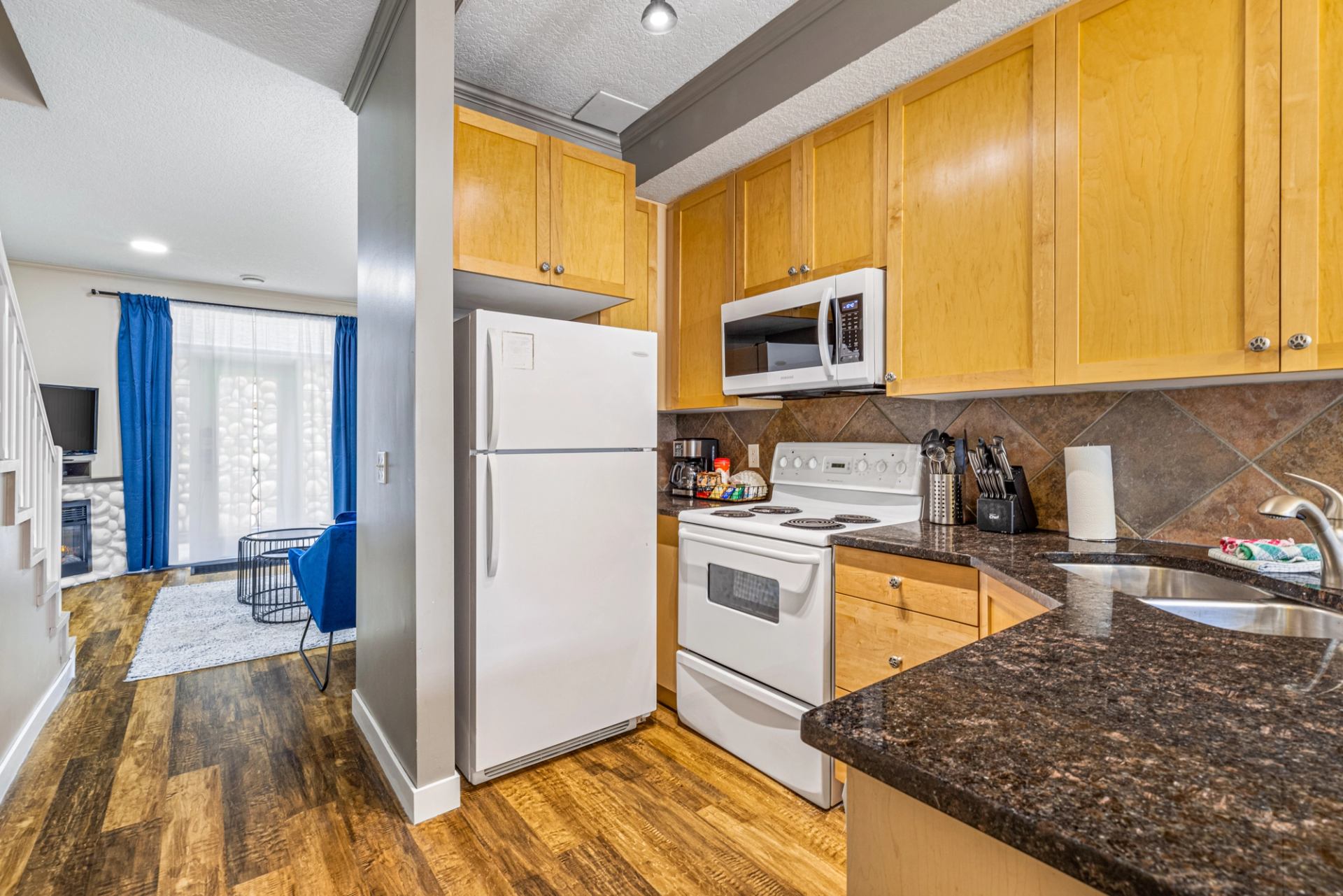 Kitchen with wood cabinets, dark counters, white appliances and adjoining living area.