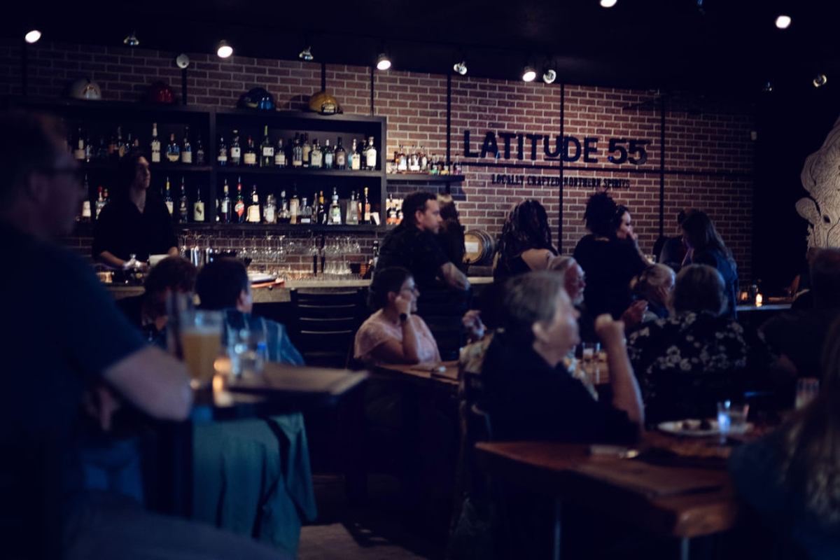 Crowded bar interior at Latitude 55 Distillery and Lounge with guests enjoying drinks.