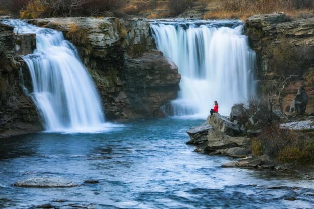 A woman sits on a rock overlooking Lundbreck Falls.