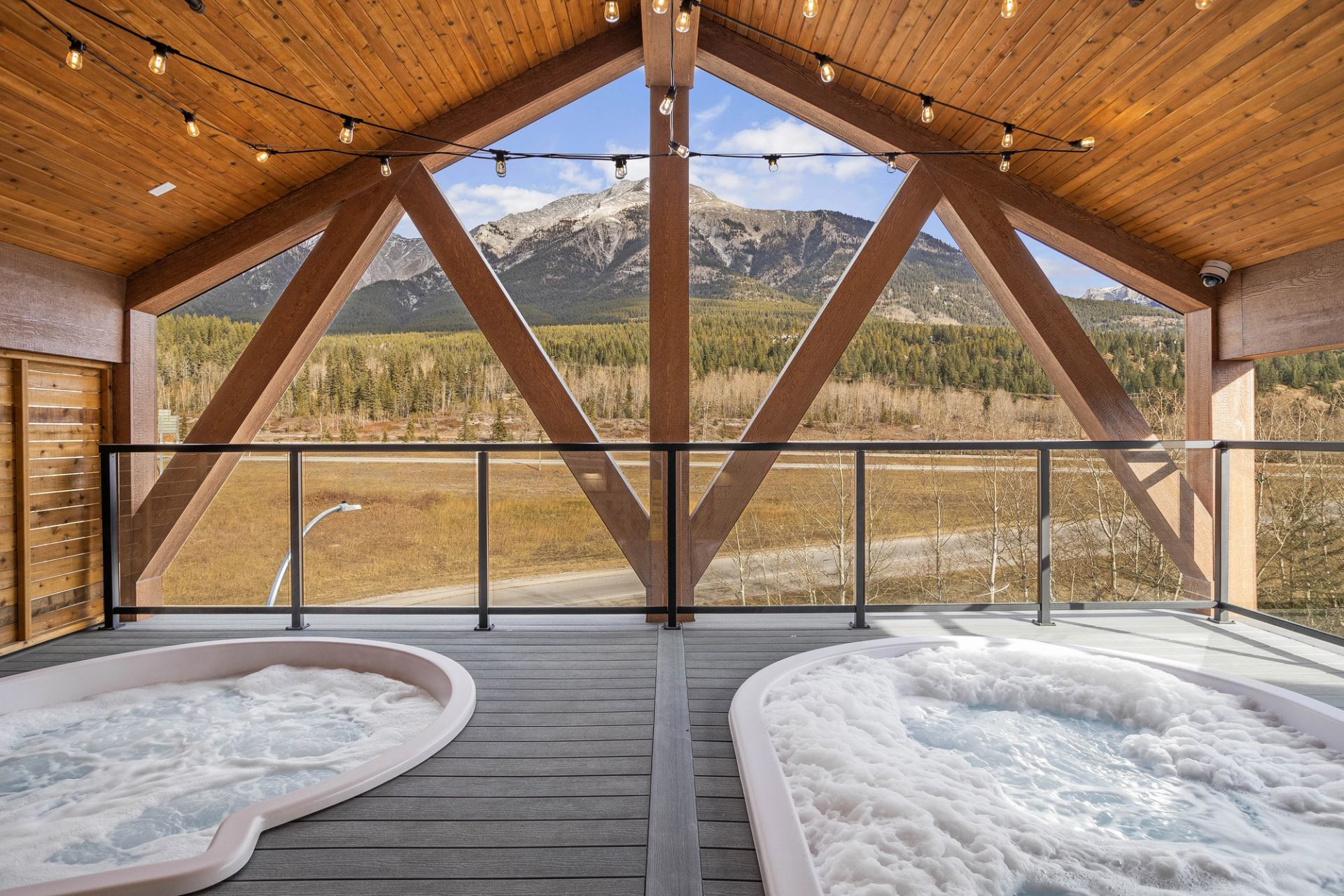 Covered deck with two bubbling hot tubs facing forested valley and mountain range.