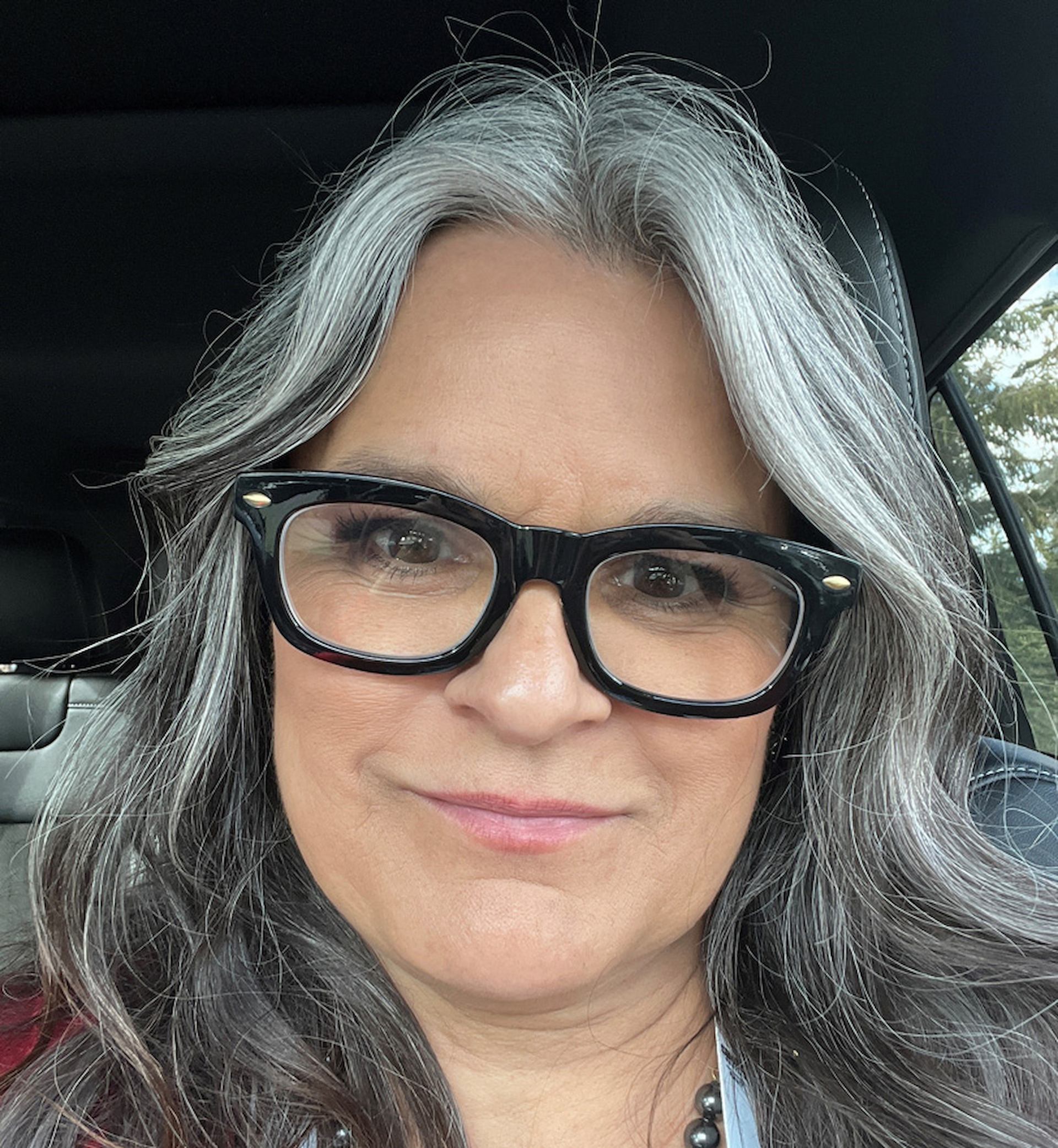 Georgina Lightning in car with long wavy hair and black-framed glasses.