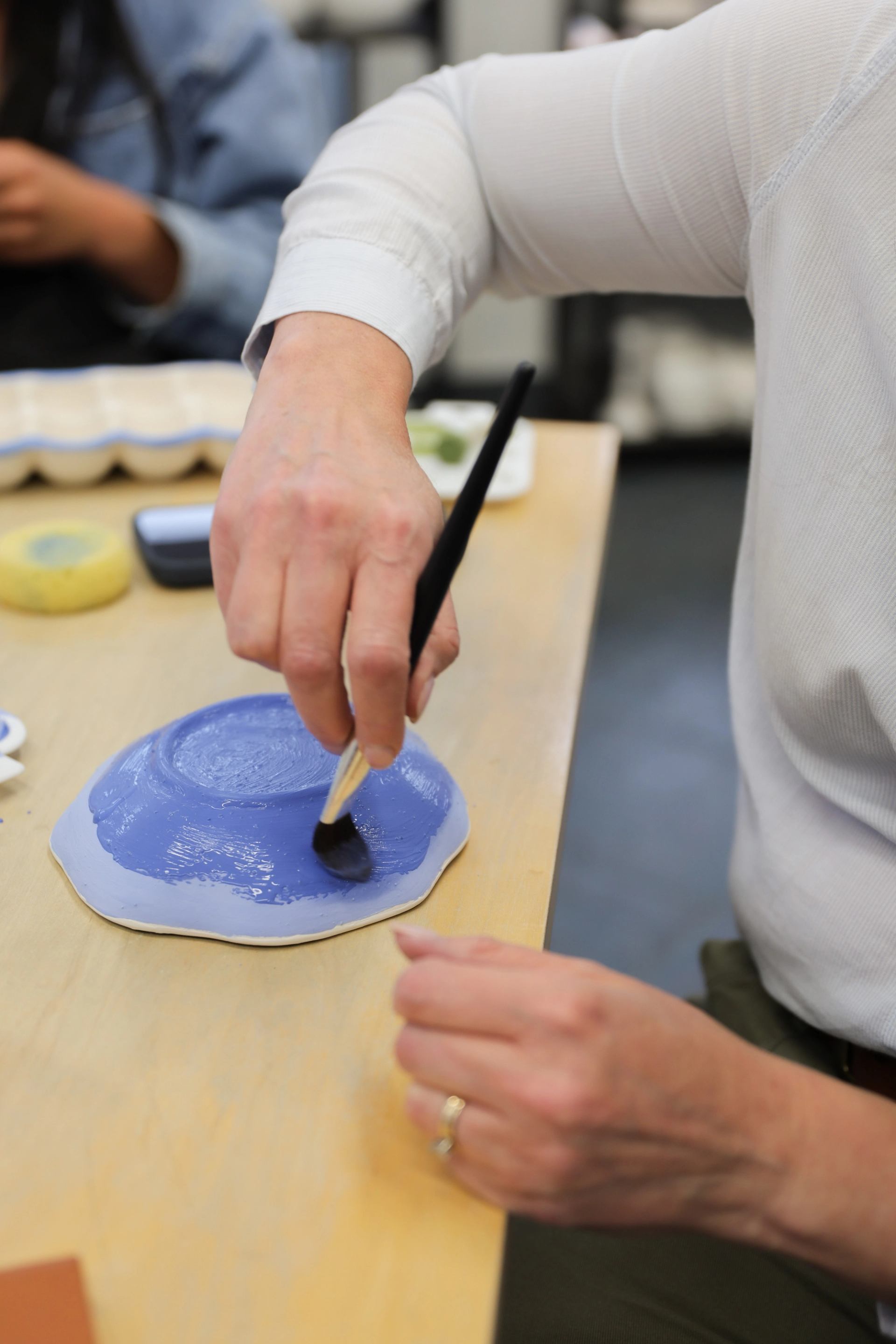 Hand paints blue glaze onto an upside-down ceramic bowl on a table.