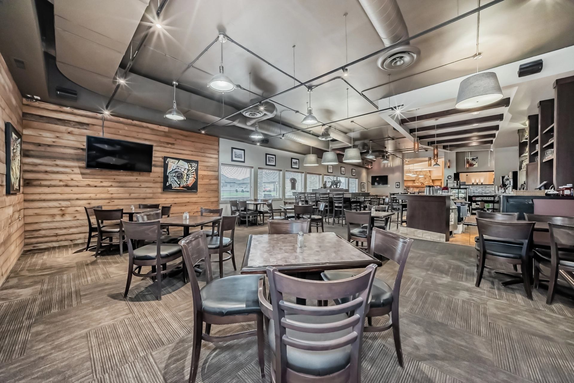 Spacious dining area with wooden walls, tables, and ceiling lights in a contemporary style