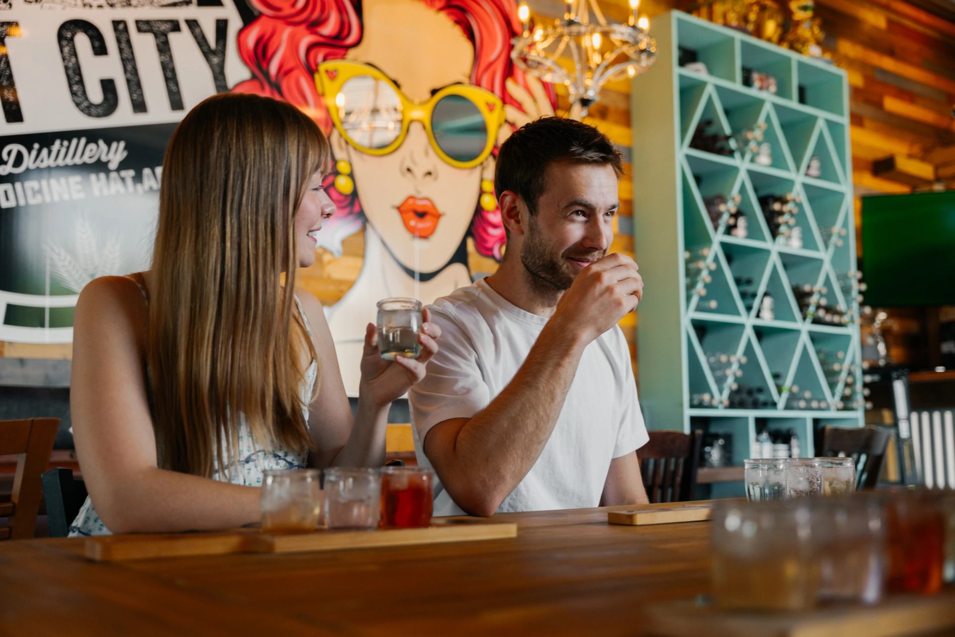 Two people seated at a bar table enjoying drinks with colorful wall art