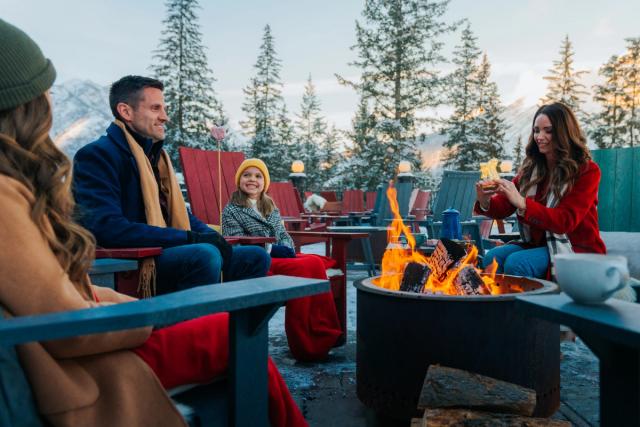 A family sitting outdoors by the fire, making s'more at the Fairmont Banff Springs Hotel.