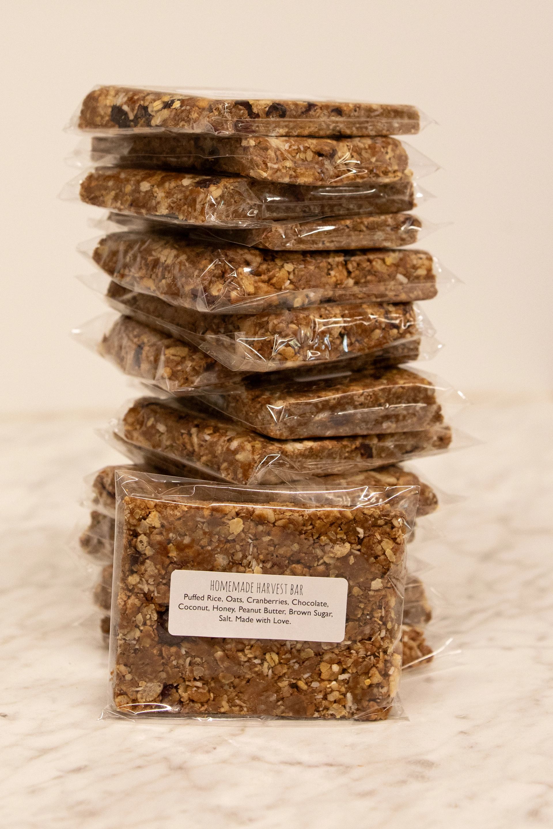 Stacked homemade harvest bars in clear plastic wrappers on a light marble surface.