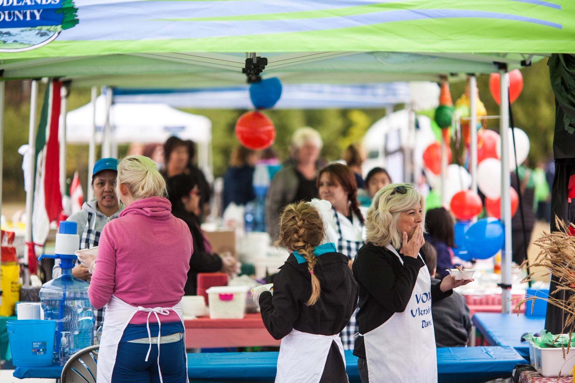 Volunteers working at a busy outdoor festival booth with food and decorations.