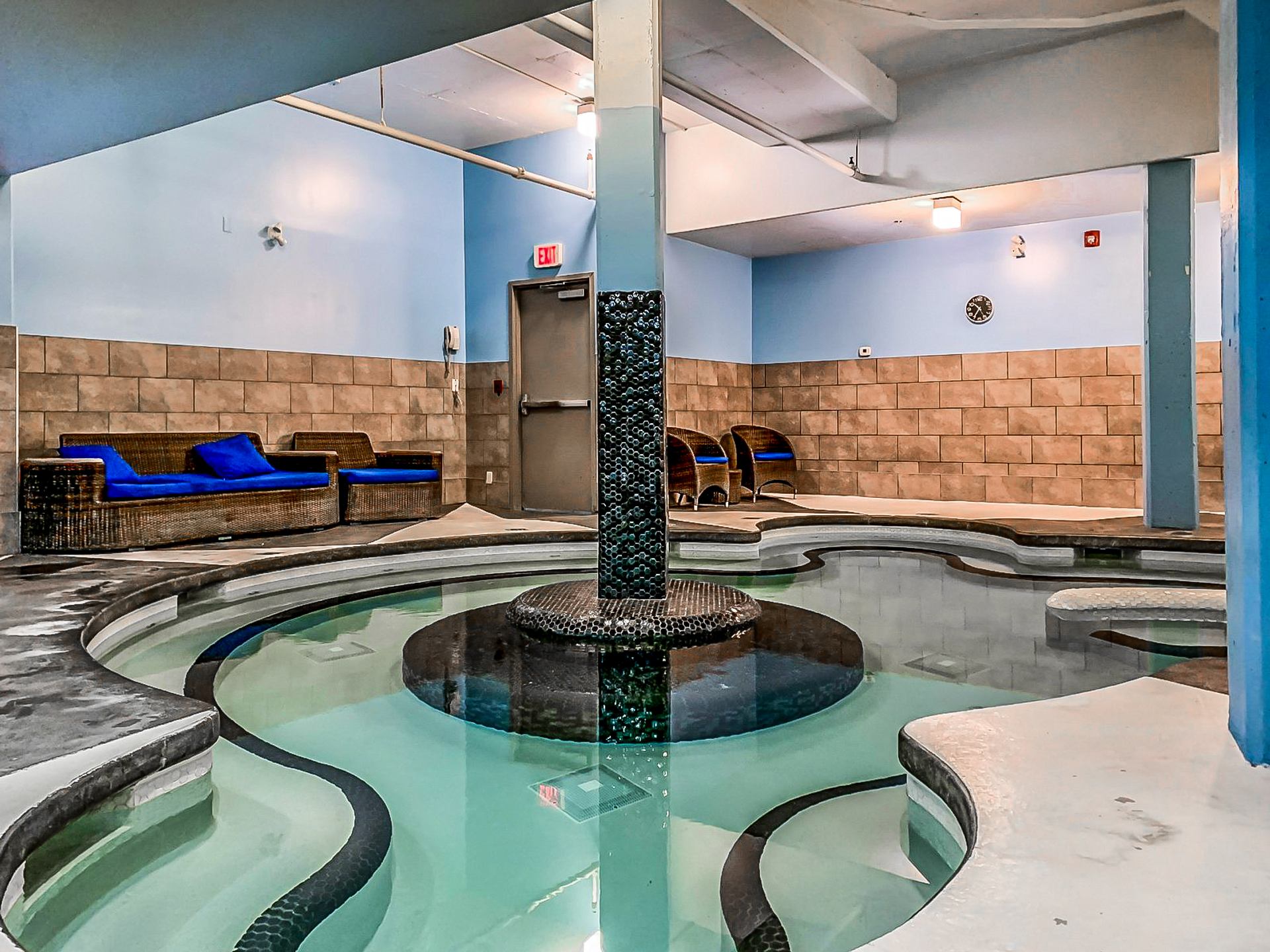 Indoor spa pool with central column, curved edges and wicker lounge seating.