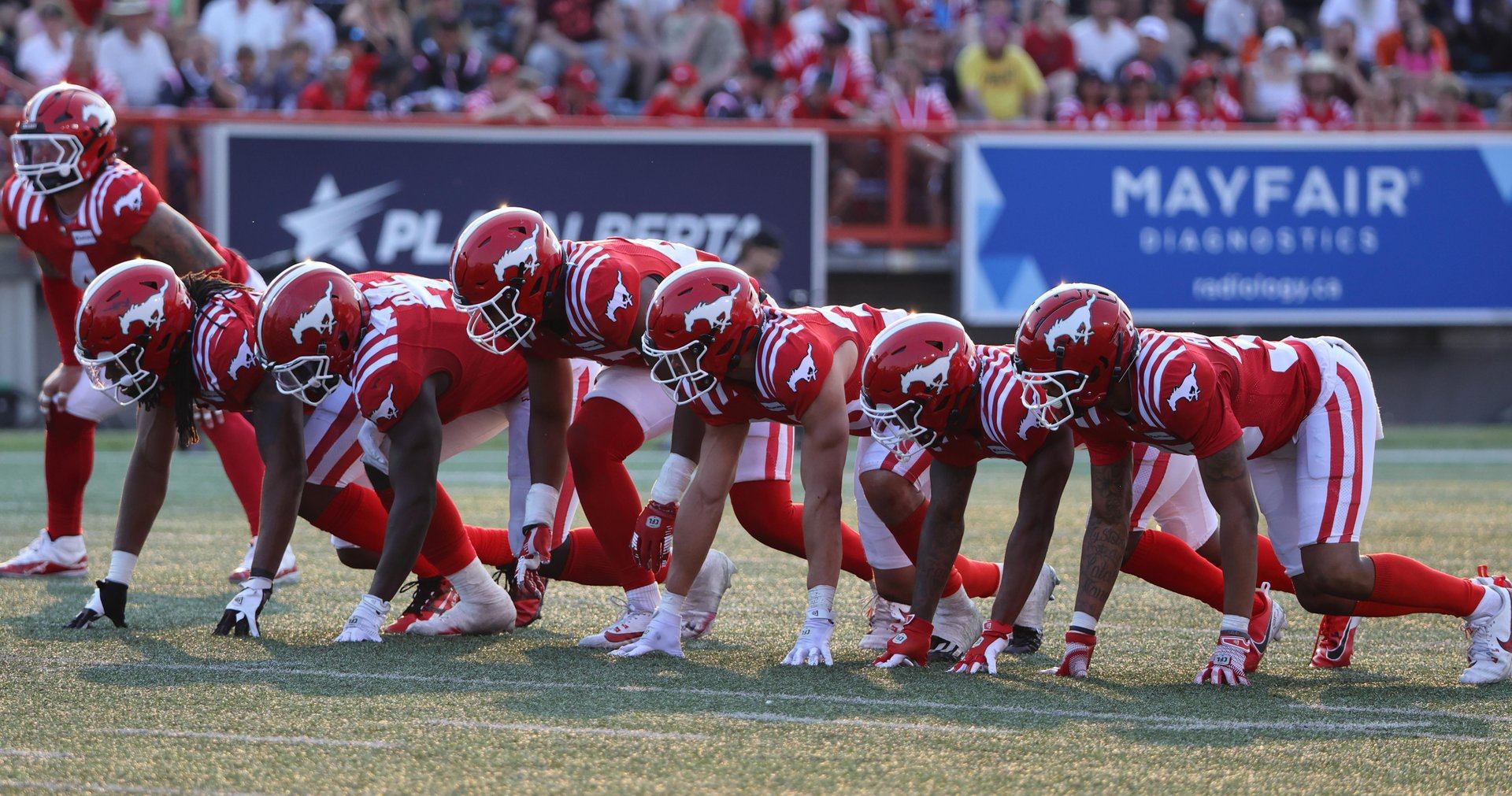 Football players in red uniforms crouch at the line of scrimmage.