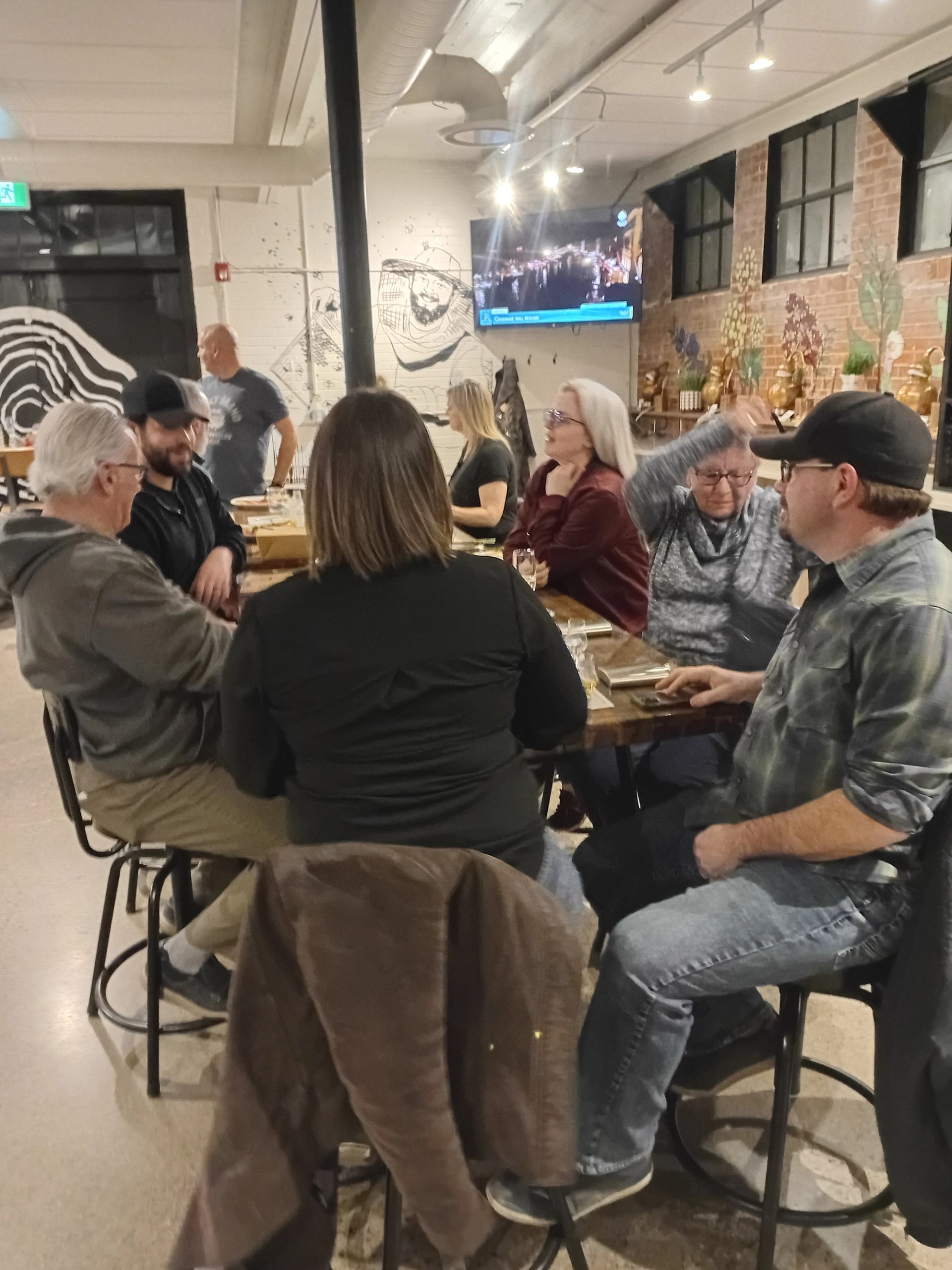 Group of people converse around a wooden table in a restaurant.