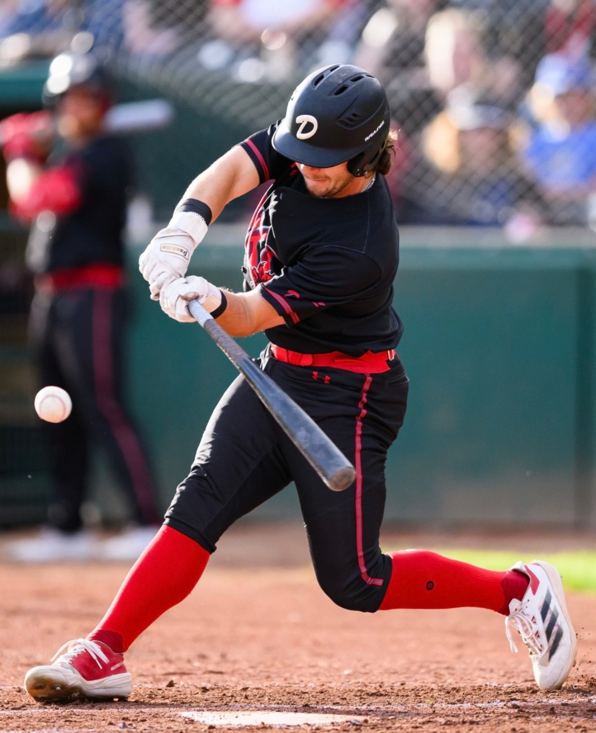 Baseball player in black and red uniform swinging at a pitch during a game.