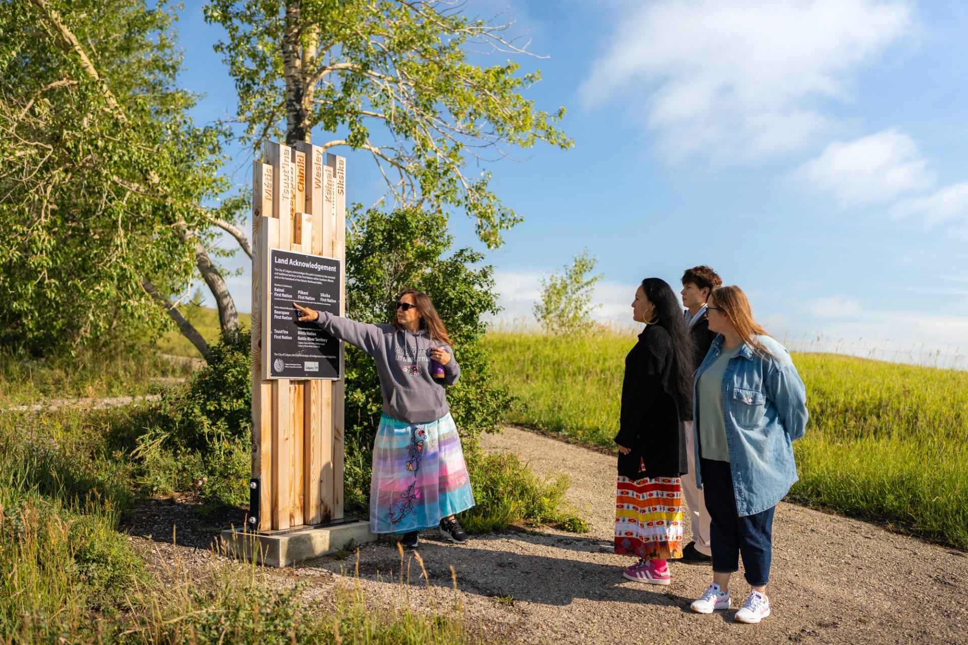 A small group stands outdoors as one person points to an informational sign.