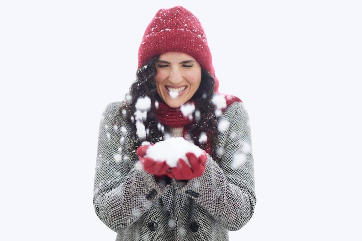 Person in red hat and gloves tosses snow from cupped hands.