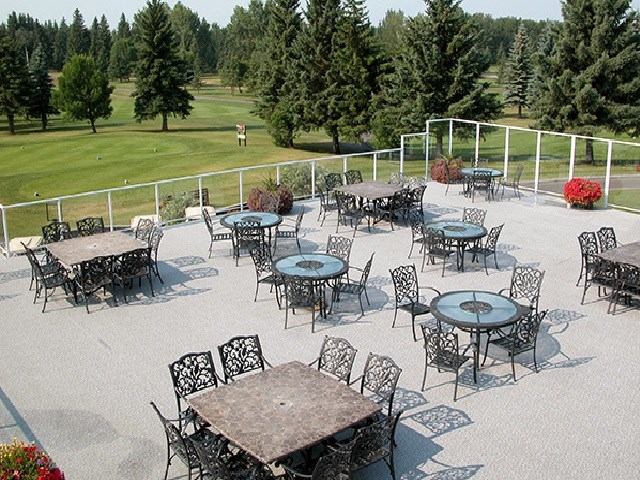 Outdoor patio area with decorative metal tables and chairs overlooking a lush green golf course surrounded by tall trees.