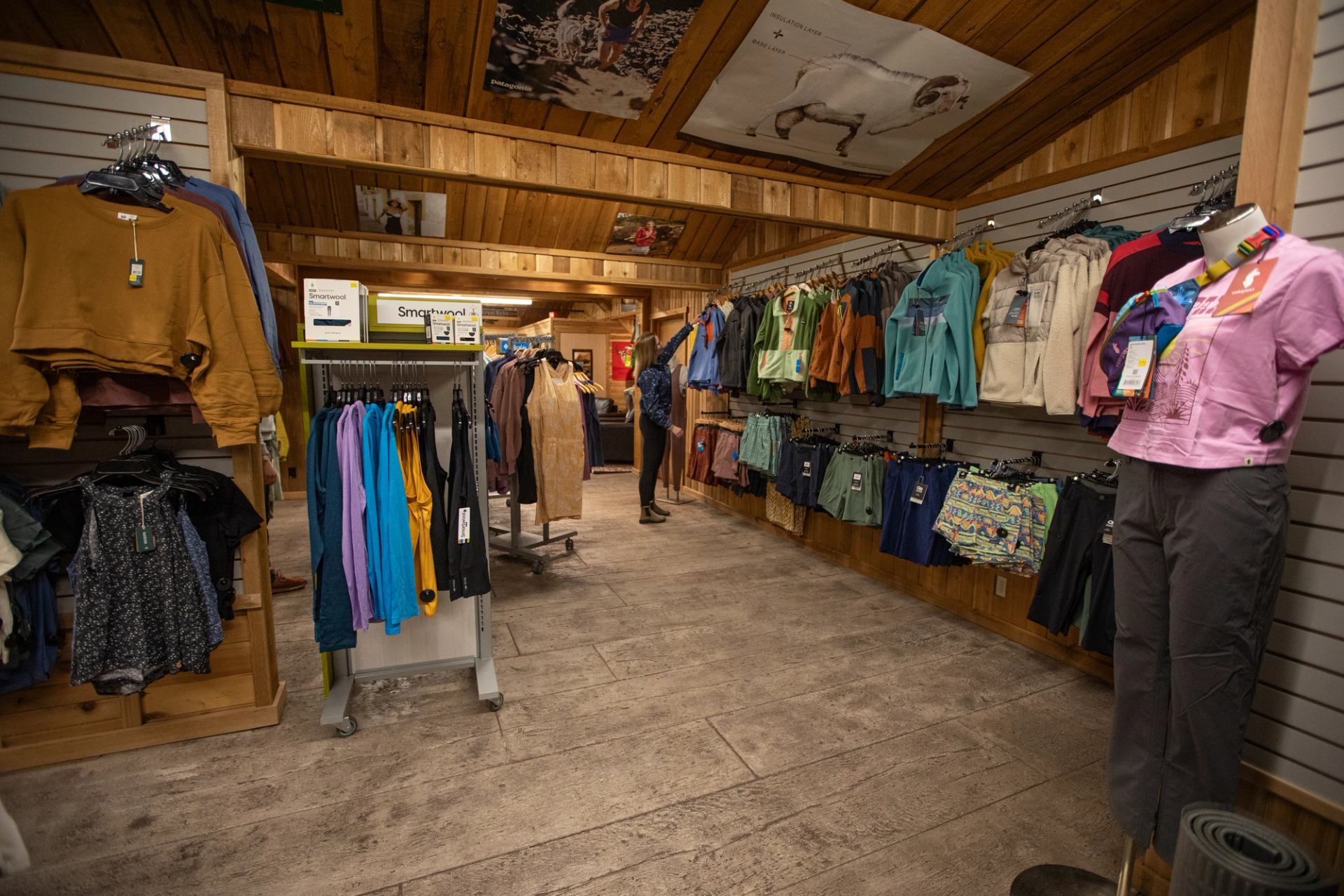 Clothing store interior with wooden walls, racks of casual wear and a browsing shopper.