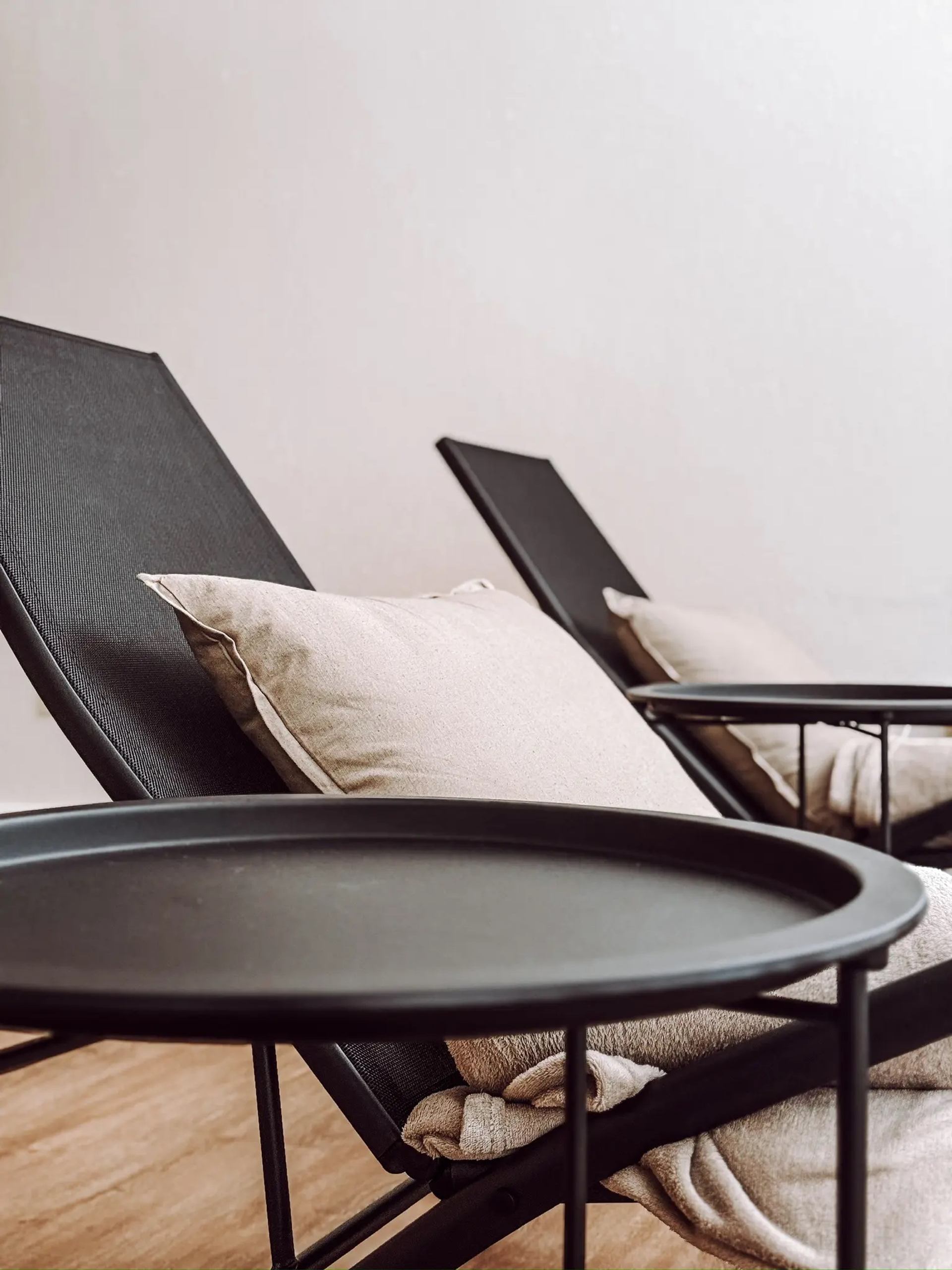 Two cushioned lounge chairs with a small round table in a peaceful spa setting.