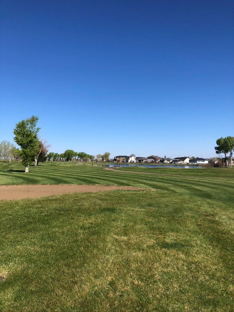 Golf fairway with a sand patch and houses in the distance under a clear blue sky.