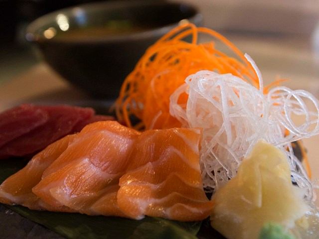 Fresh sashimi slices with shredded garnish and wasabi on a dark platter at Kuma Yama.