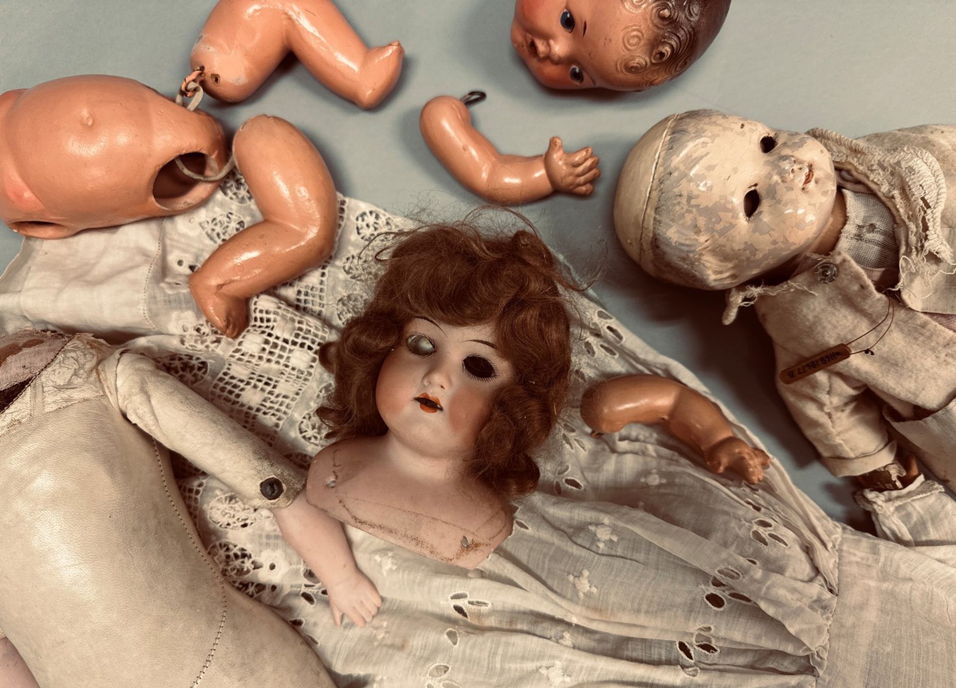 Antique dolls and detached doll parts lie on white lace fabric.