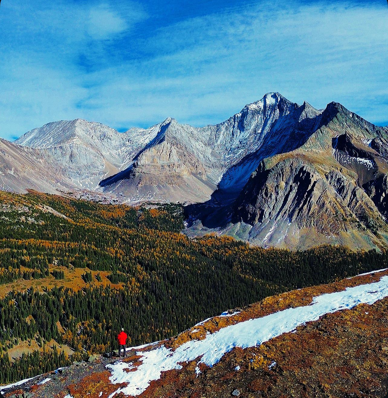 Hiker overlooks rugged peaks and forested valleys in Rockies