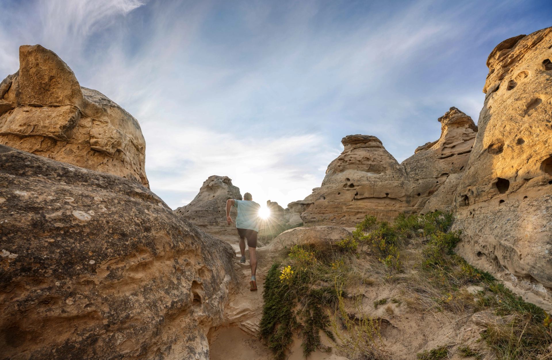 A person running through the hoodoos while the sun peaks through at Writing-On-Stone Provincial Park in Southern Alberta.