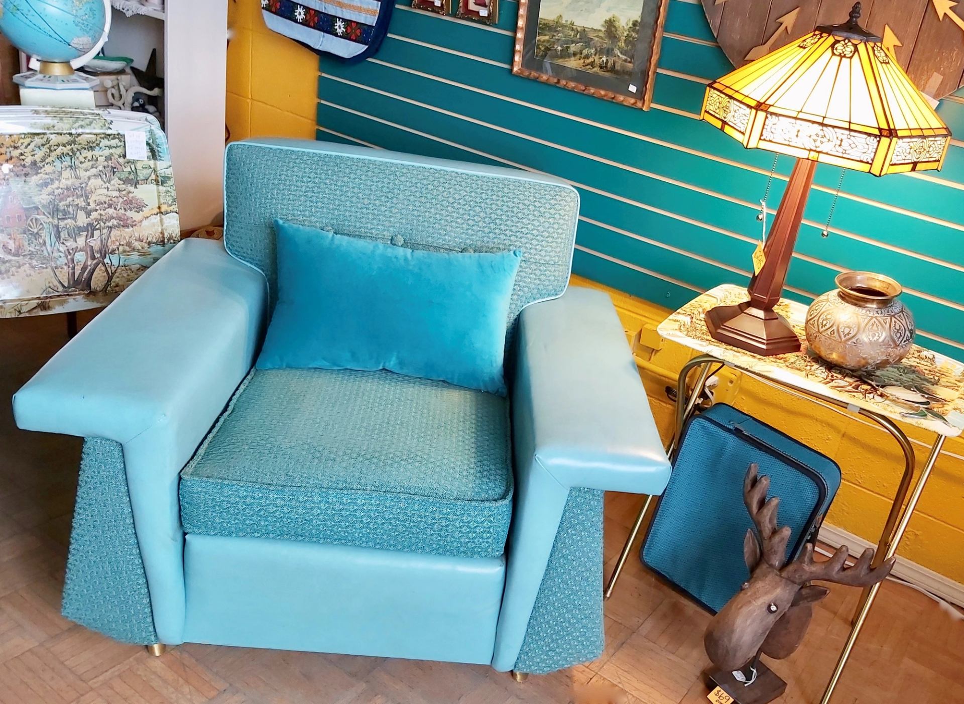 Blue armchair with pillow beside table lamp, moose head decor and globe.