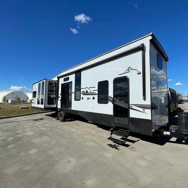 Large RV with slide-outs and mountain graphics parked under blue sky on paved lot.
