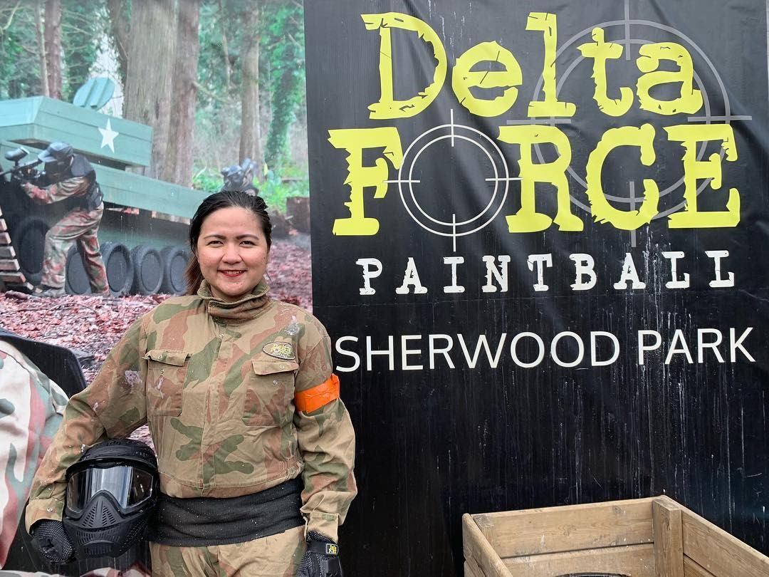 Person in camouflage holds paintball mask beside Delta Force Paintball Sherwood Park sign.