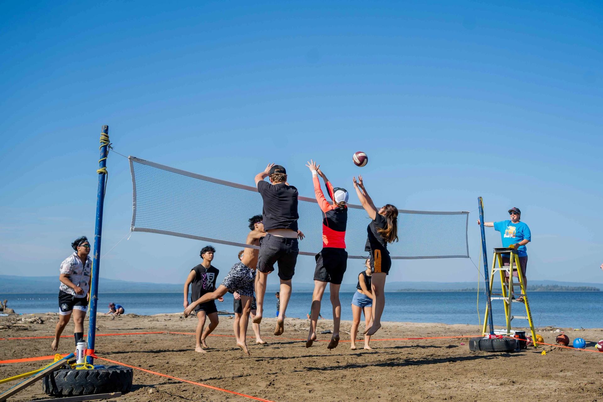 Group of young adults play energetic beach volleyball on a sunny day as a referee watches the action closely.
