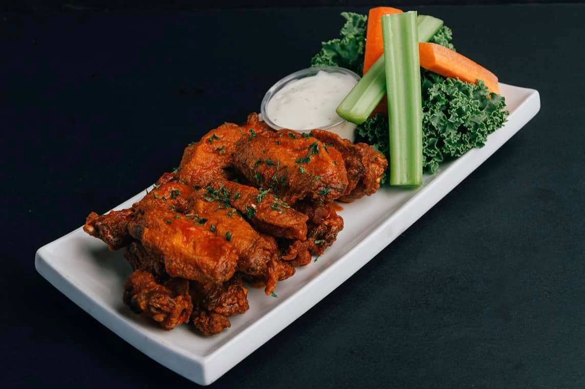 A platter of chicken wings is served with celery, carrots, leafy greens, and dipping sauce.