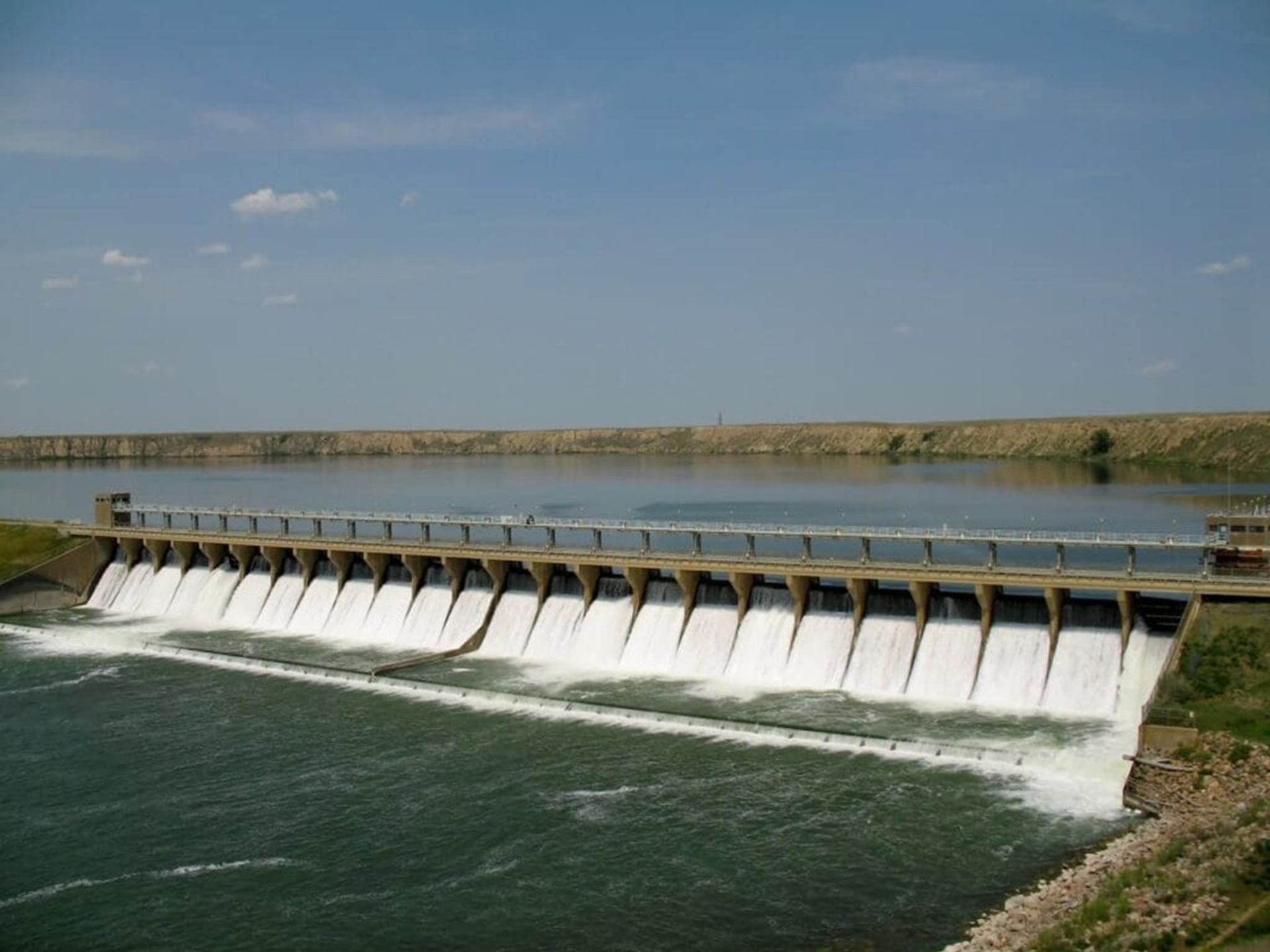 Concrete hydroelectric dam releases water into river below, with calm reservoir behind.