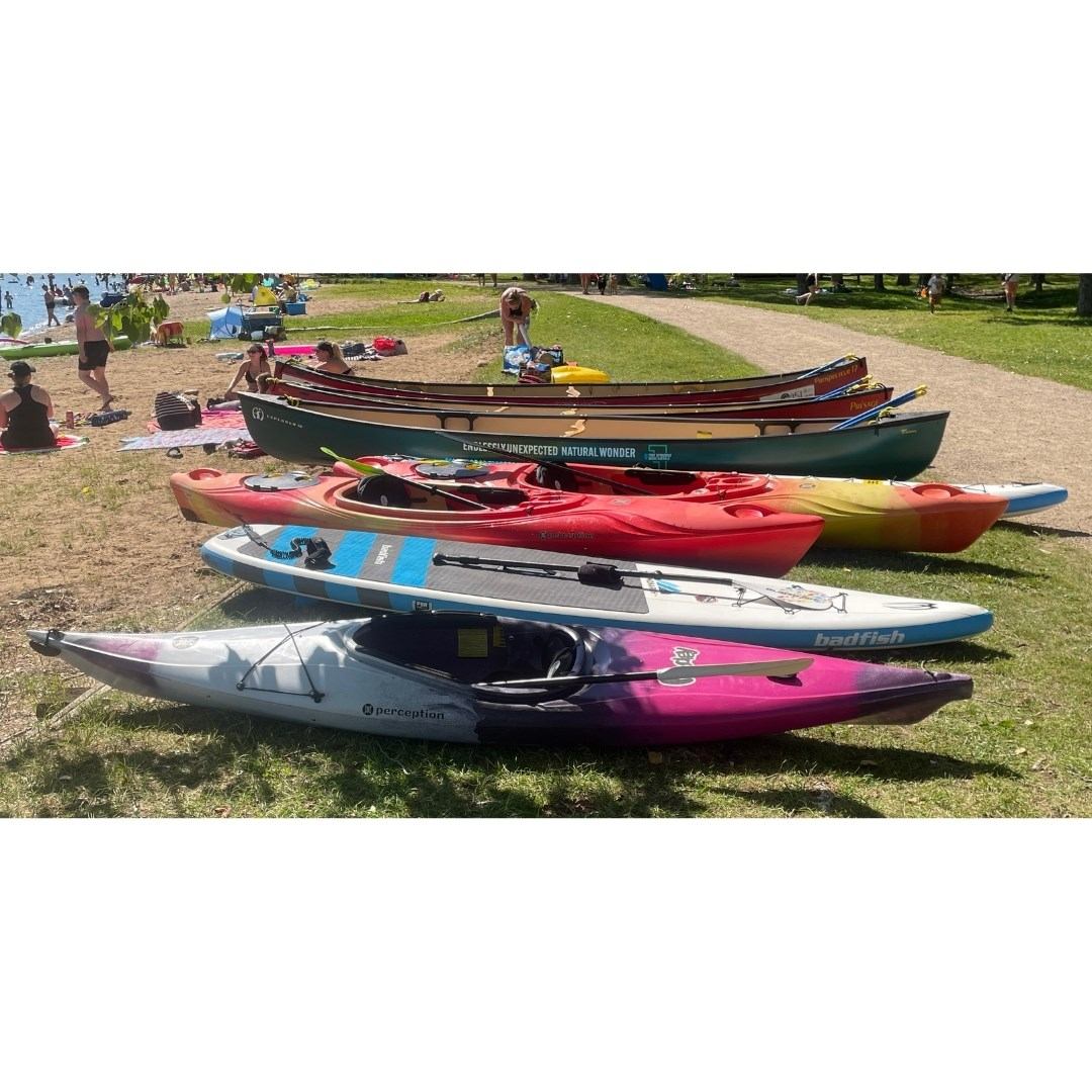 Kayaks and canoes lined up on grass near water, ready for outdoor use.