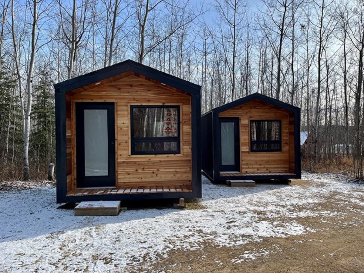 Two small wooden cabins in a snowy forest clearing.