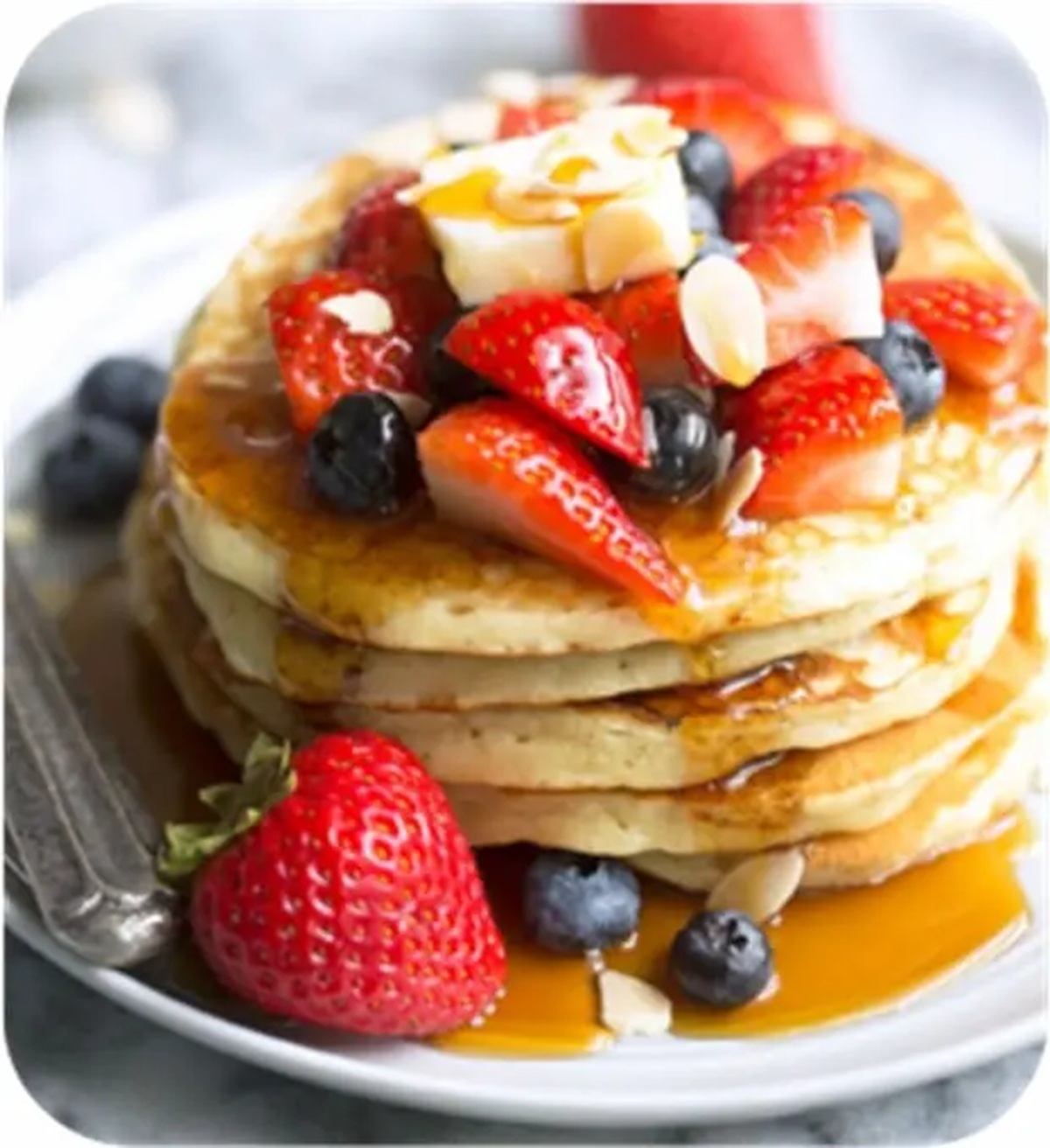 Stack of pancakes with strawberries, blueberries, butter and syrup on a white plate.