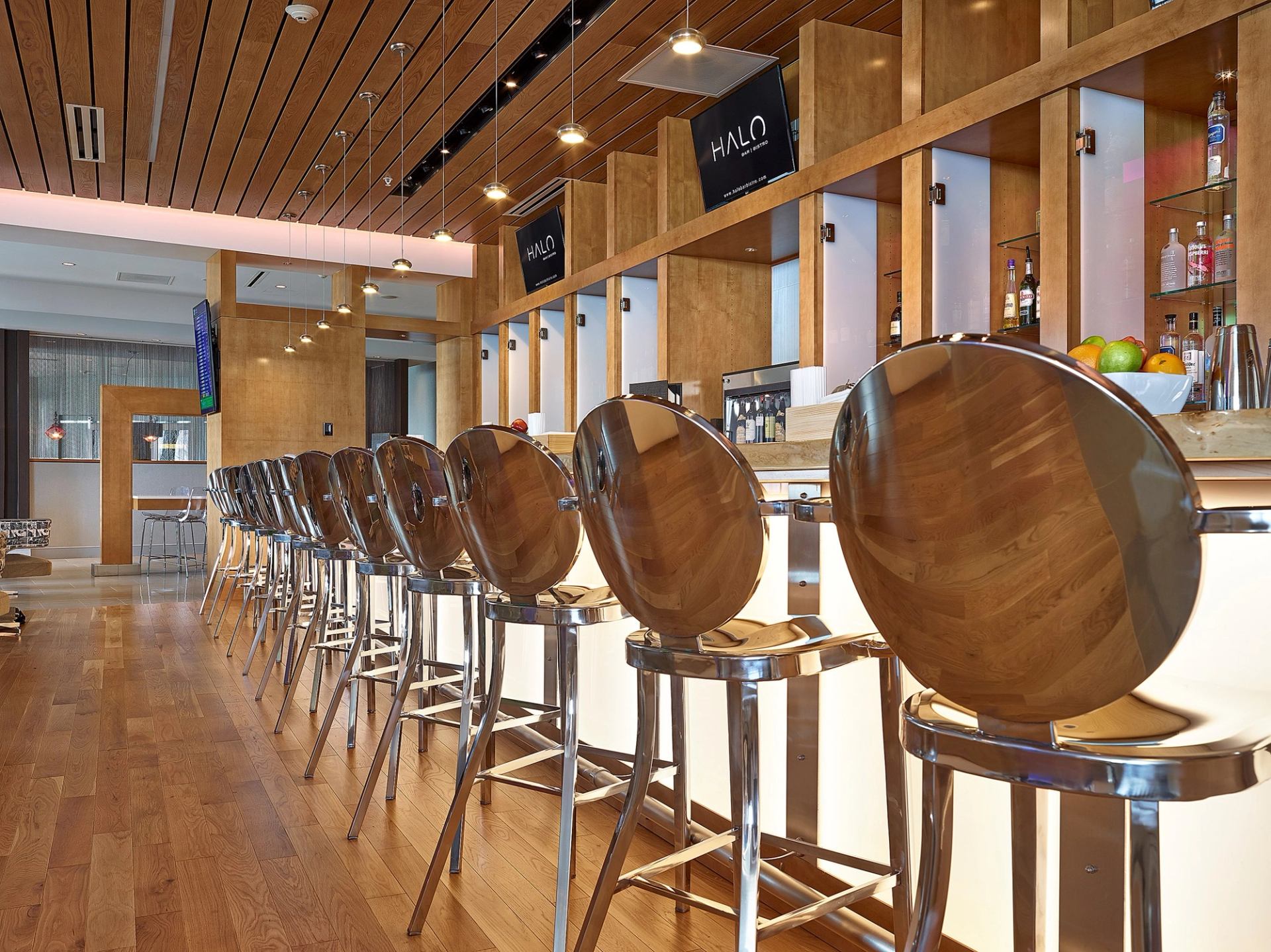 Modern bar with wood-accented stools, warm lighting, and stocked shelves at HALO Bar|Bistro.