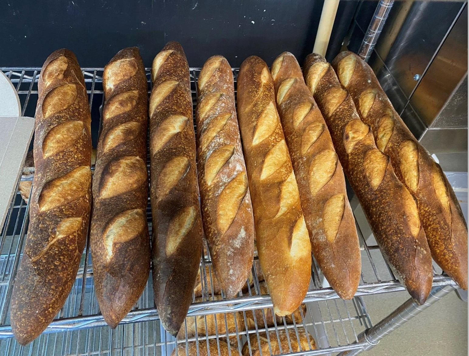 Fresh loaves of bread cooling on metal racks in a bakery kitchen.